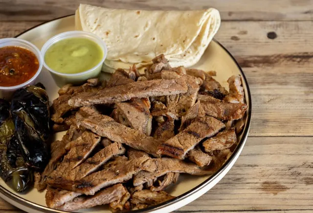 Plato de carne asada en tiras con tortillas y salsas