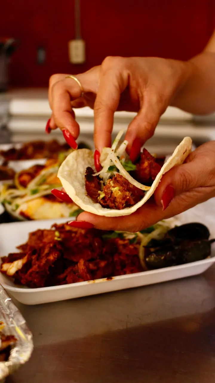 Manos armando un taco con carne, cebolla y cilantro