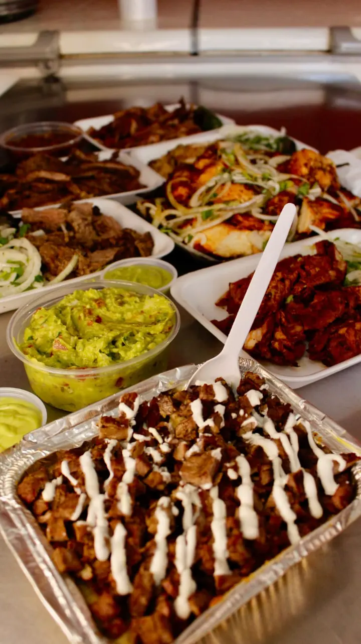 Mesa con charolas de carne y pollo asado, guacamole y una charola de carne picada con crema