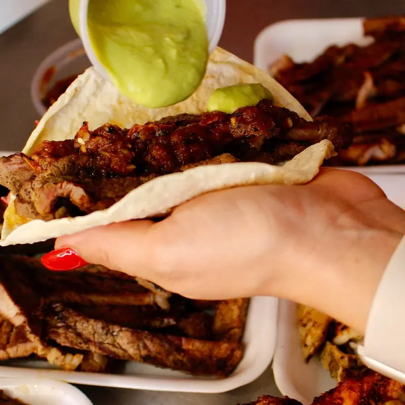 Taco de carne asada con salsa roja mientras le sirven salsa verde